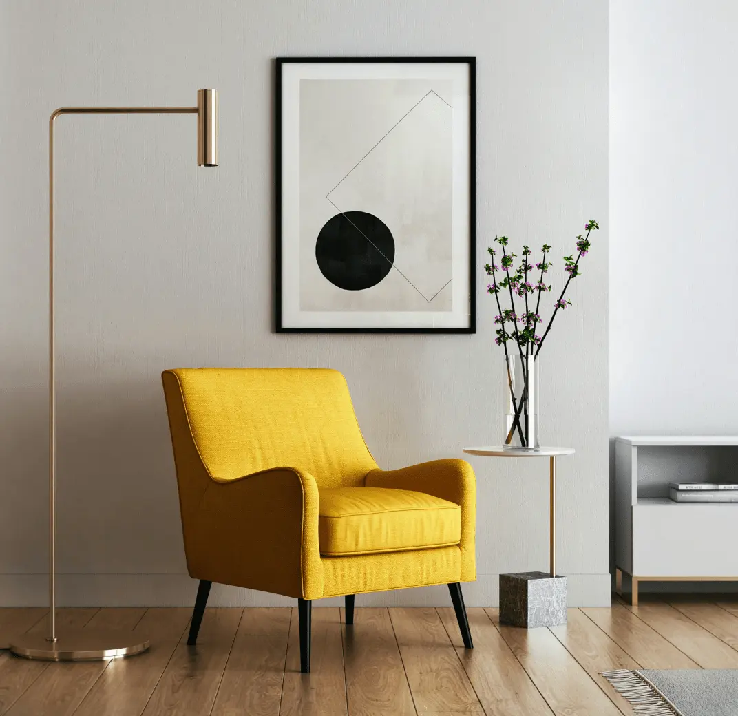 A cozy reading nook with a yellow armchair, a floor lamp, and a framed abstract print.